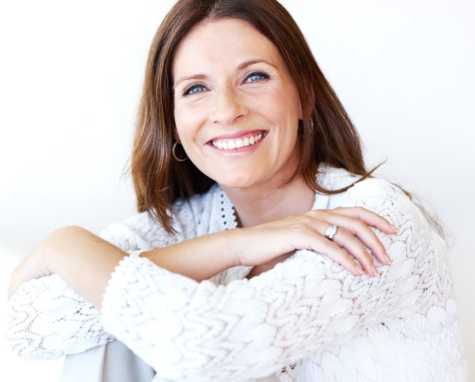 Smiling woman in white sweater with her hands over her knees