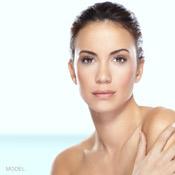 Close-up of woman with brown slicked-back hair, her right hand touching her bare left shoulder as she looks at the camera.