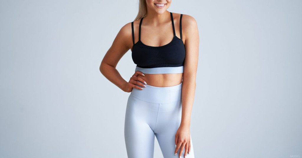 Body confident woman posing in gym clothes after liposuction (model)