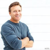 Man in blue crewneck sweater crosses his arms in front of him and smiles at the camera.
