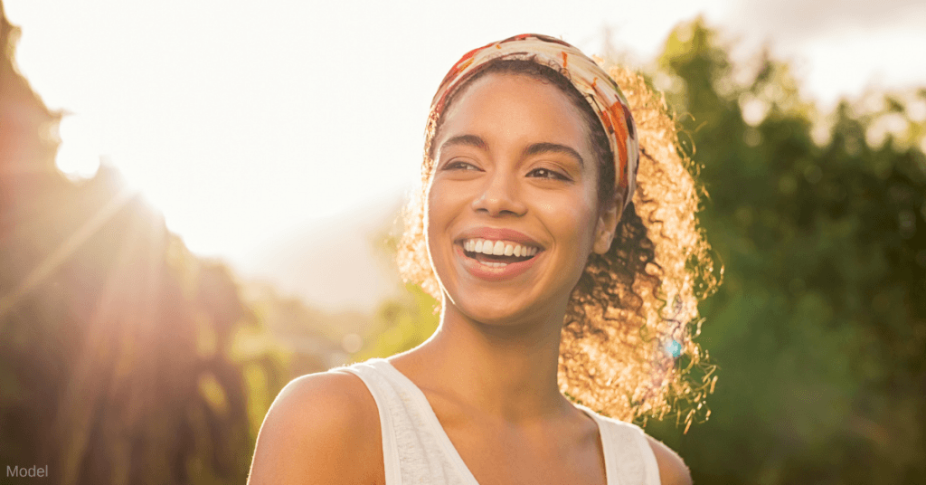 Close up photo of a woman (model) standing outside and smiling in the sunshine