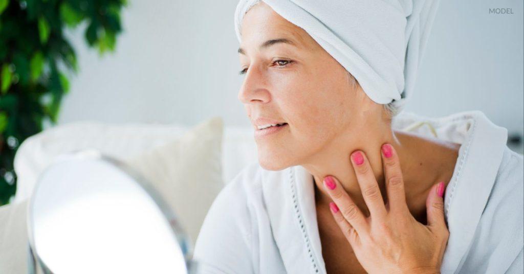 Woman with smooth, youthful skin under her chin (model) looking in the mirror.