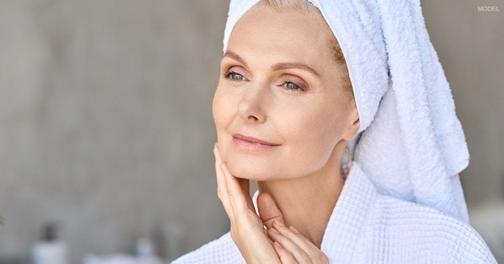 Woman with a chiseled jawline (model) looks at the camera with a hand rested under her chin.