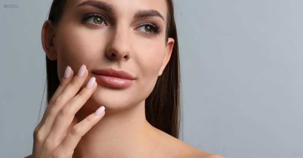 Woman with plump lips (model) holds a hand up to her face.