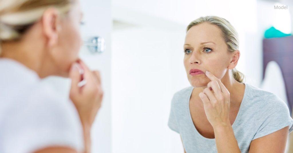 Woman (model) examining her face in the mirror.